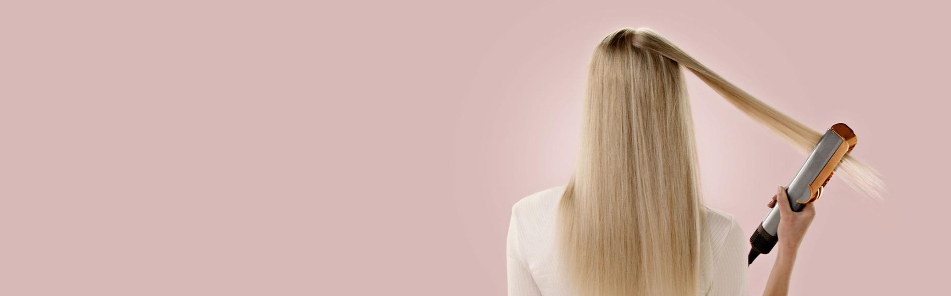 Model with long, blonde hair straightening the back of her hair with the Dyson Airstrait straightener.